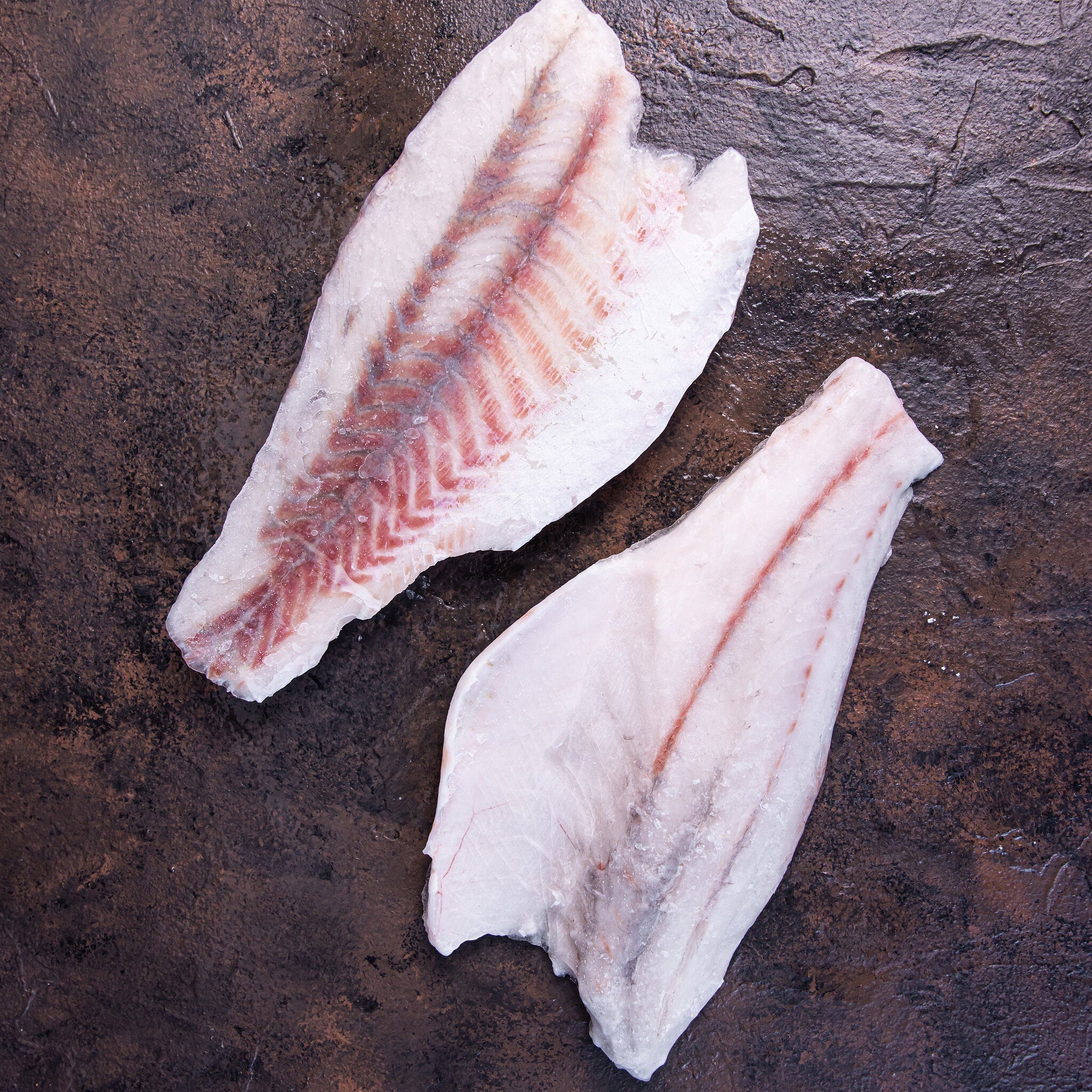 Frozen skinless boneless barramundi fillets on dark stone